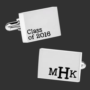 Könnte beinhalten: Zwei silberne rechteckige Manschettenknöpfe. Ein Manschettenknopf hat den Text "Class of 2016" in Schwarz. Der andere Manschettenknopf hat die Initialen "MHK" in Schwarz. Die Manschettenknöpfe sind auf dunklem Hintergrund.