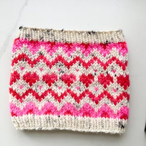 May include: A knitted headband with a white base and a pink and red geometric pattern.