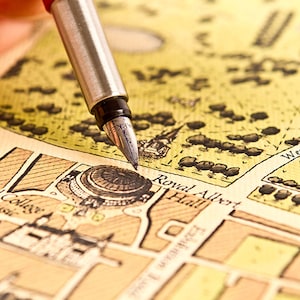 May include: A close-up of a vintage map with a fountain pen pointing to the location of "Royal Albert Hall".