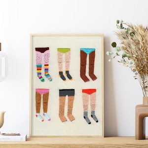 May include: A framed embroidery art print featuring six pairs of legs wearing different coloured underwear and socks. The legs are hairy and the artwork is in a minimalist style.