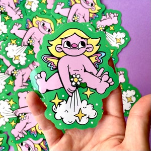 Peut inclure: Un autocollant représentant un ange de dessin animé rose avec des ailes arc-en-ciel, tenant une fleur et libérant un nuage de fumée blanche. L'ange est sur un fond vert avec des étoiles jaunes.