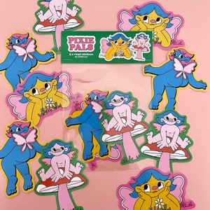 May include: A collection of colorful vinyl stickers featuring whimsical fairy characters. The fairies have blue and yellow skin, pink wings, and are posed on mushrooms or with flowers. The stickers are packaged in a clear plastic sleeve with the text "Pixie Pals".