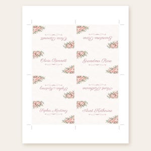 May include: A sheet of eight rectangular place cards featuring a cream background with pink floral corner accents. Each card displays names in a cursive script, including Olivia Bennett, Grandma Rose, Sophia Martinez, and Aunt Katherine.