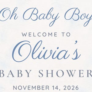 以下が含まれることがあります： 水色の水彩画風の背景を持つ長方形のサイン。Oh Baby Boy、WELCOME TO、Olivia's、BABY SHOWER、NOVEMBER 14, 2026という文字が、青い筆記体とグレーのセリフ体のフォントを組み合わせて記載されています。
