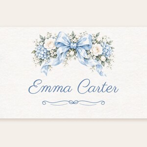 May include: A rectangular card featuring a watercolor illustration of a light blue ribbon bow centered above a floral arrangement of white roses and blue hydrangeas. The name Emma Carter is printed in blue script below the flowers.