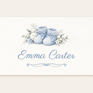 May include: A rectangular card featuring a watercolor illustration of a pair of light blue knitted baby booties surrounded by white and blue flowers and green leaves. The name Emma Carter is printed in blue script below the booties.