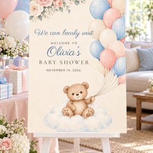 May include: A rectangular baby shower welcome sign on a white easel featuring a watercolor illustration of a brown teddy bear sitting on a cloud, holding a bunch of pink, blue, and cream balloons. Text reads: We can bearly wait, WELCOME TO Olivia's BABY SHOWER, NOVEMBER 14, 2026, with pink and white floral accents.