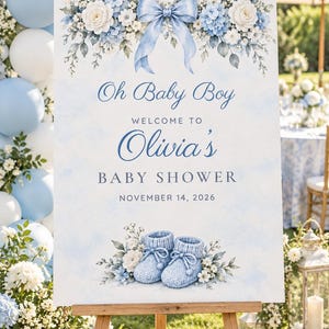 Pu&ograve; includere: Un cartello di benvenuto rettangolare per un baby shower con sfondo acquerello azzurro, una composizione floreale con un fiocco blu centrale e il testo Oh Baby Boy Welcome to Olivia's Baby Shower November 14, 2026, con scarpine da neonato blu.
