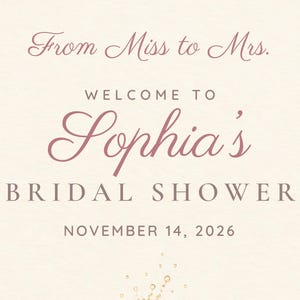 May include: A cream-colored sign featuring the text From Miss to Mrs. WELCOME TO Sophia's BRIDAL SHOWER NOVEMBER 14, 2026 in dark pink and brown lettering, accented with delicate floral illustrations at the top and bottom corners.