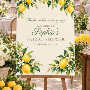 May include: A rectangular welcome sign for a bridal shower on a wooden easel, featuring watercolor illustrations of yellow lemons and white blossoms. The text reads: She found her main squeeze, WELCOME TO Sophia's BRIDAL SHOWER, NOVEMBER 14, 2026.