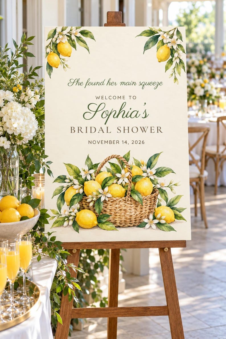 May include: A rectangular sign on a wooden easel featuring watercolor illustrations of lemons and white blossoms. The text reads: She found her main squeeze, WELCOME TO Sophia's BRIDAL SHOWER, NOVEMBER 14, 2026, with a basket of lemons.