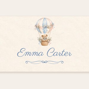 May include: A rectangular card featuring a watercolour illustration of a teddy bear in a blue and beige hot air balloon decorated with flowers. Below the illustration, the name Emma Carter is printed in blue script, followed by a decorative line.
