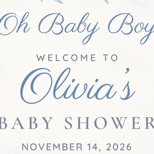 以下が含まれることがあります： Oh Baby Boy WELCOME TO Olivia's BABY SHOWER NOVEMBER 14, 2026と青い文字で書かれた白い看板。長方形のカードの上下の端には、青い水彩画風の花のアクセントが施されています。