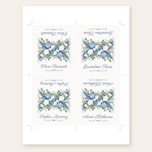May include: A sheet of four rectangular paper labels featuring a floral arrangement of blue delphiniums and white roses. Each label displays a name in blue script: Olivia Bennett, Grandma Rose, Sophia Martinez, and Aunt Katherine.