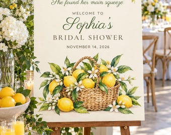 May include: A rectangular sign on a wooden easel featuring a watercolor illustration of lemons and white blossoms. The text reads: She found her main squeeze, WELCOME TO Sophia's BRIDAL SHOWER, NOVEMBER 14, 2026. A woven basket filled with lemons sits at the base.