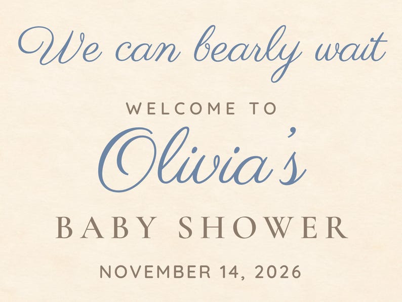 May include: A cream-colored sign with blue and brown text that reads: We can bearly wait, WELCOME TO, Olivia's, BABY SHOWER, NOVEMBER 14, 2026. The text uses a mix of elegant cursive script and clean, capitalized sans-serif typography.