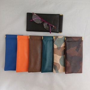 May include: Assortment of seven eyeglass cases in various colors and patterns. The cases are made of leather and have gold metal accents. The cases are lined up in a row on a white surface.