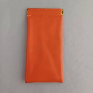 May include: A bright orange leather glasses case with a gold metal clasp.