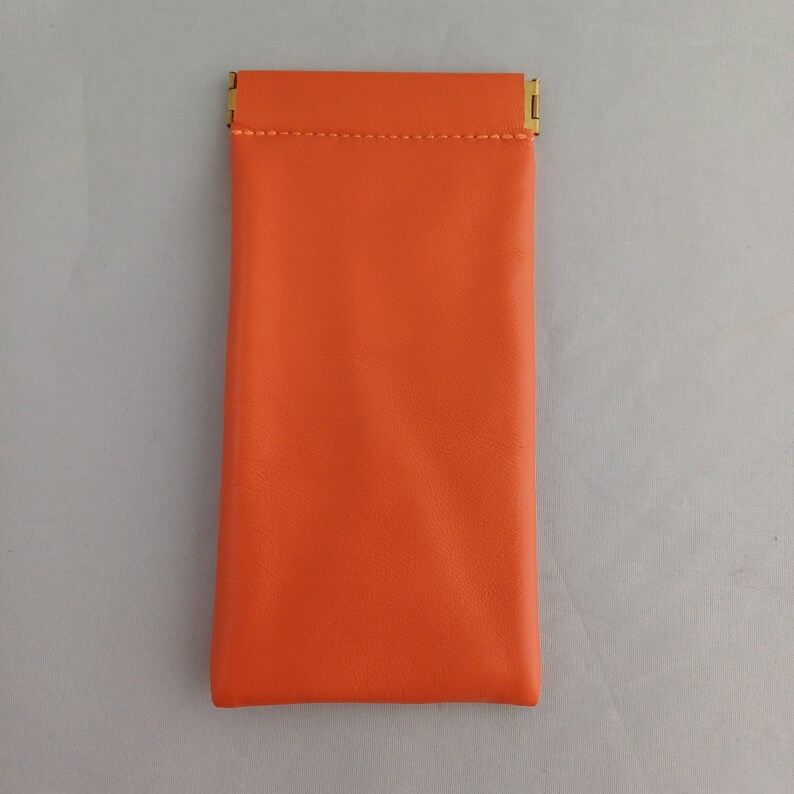 May include: A bright orange leather glasses case with a gold metal clasp.