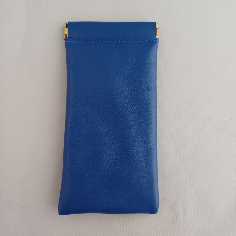 May include: A blue leather case with gold metal clasps. The case is designed to hold small items like glasses or jewelry.