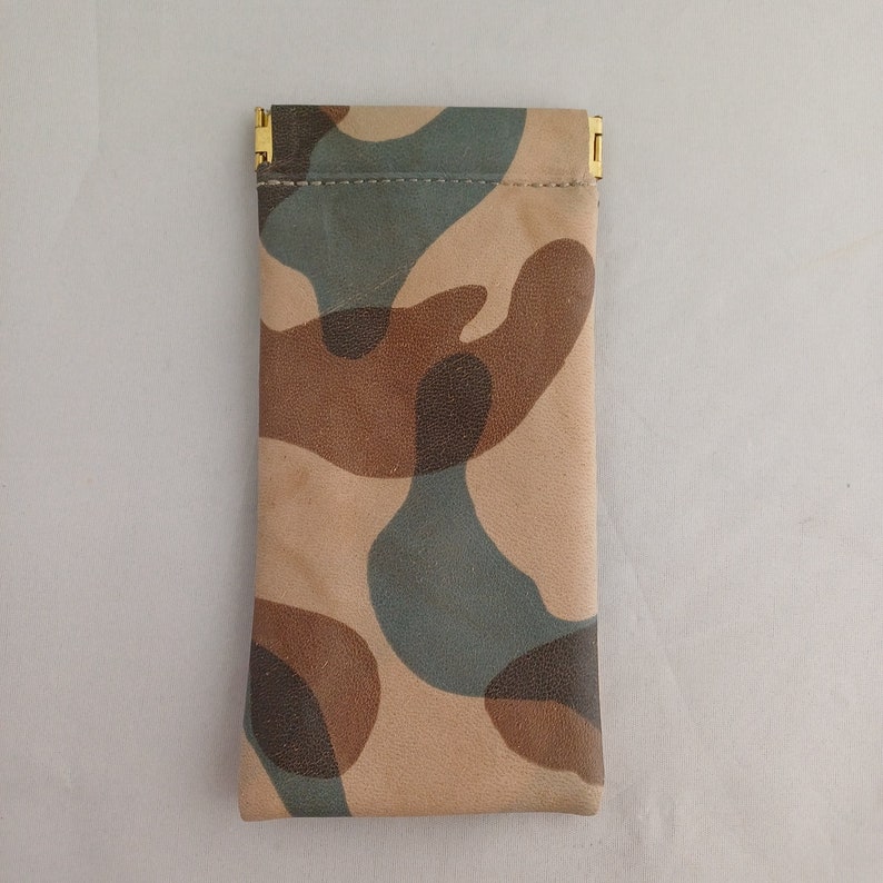 May include: A camouflage-patterned pouch with a gold zipper closure. The pouch is made of a soft, textured material.