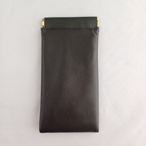 May include: A black leather case with a gold zipper closure. The case is designed to hold small items, such as glasses or jewelry.