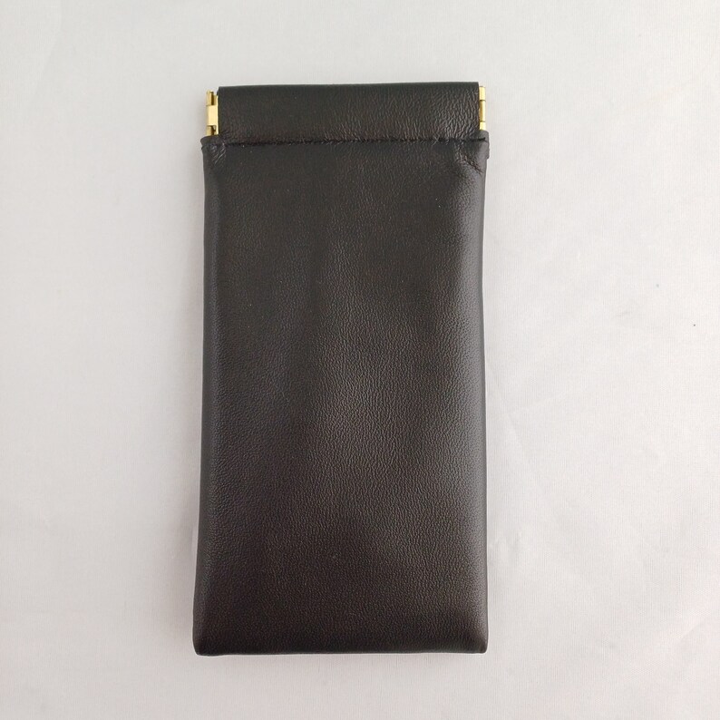 May include: A black leather case with a gold zipper closure. The case is designed to hold small items, such as glasses or jewelry.