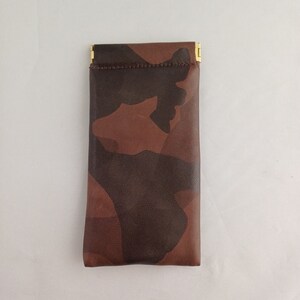 May include: A brown leather glasses case with a camouflage pattern. The case has a gold metal clasp.