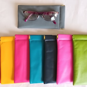 May include: Assortment of ten eyeglass cases in various colors, including red, yellow, pink, teal, navy blue, hot pink, and green. The cases are made of leather and have gold accents.
