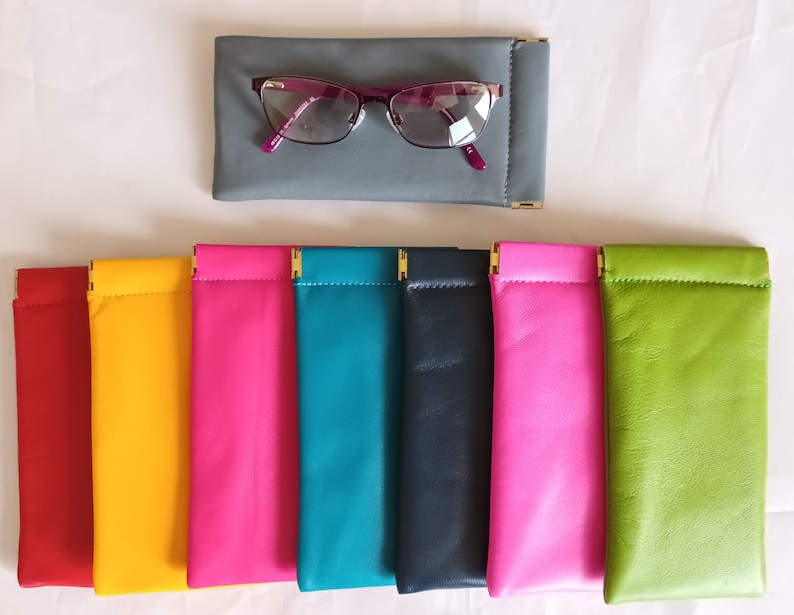 Op de afbeelding: Assortiment van tien brillenetuis in verschillende kleuren, waaronder rood, geel, roze, teal, donkerblauw, felroze en groen. De etuis zijn gemaakt van leer en hebben gouden accenten.