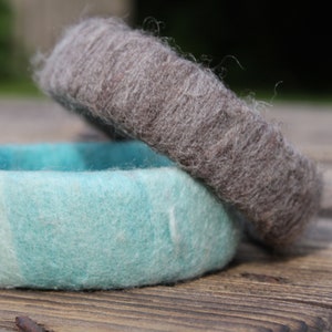 Könnte beinhalten: Zwei gefilzte Woll-Armbänder, eines in hellblau und das andere in dunkelgrau. Die Armbänder liegen übereinander.