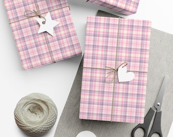 May include: Three rectangular gifts wrapped in pink, white, and lavender plaid paper. Each gift is tied with brown twine and features a white paper tag in the shape of a star or heart. A ball of twine and black scissors are nearby.
