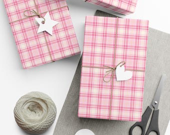 May include: Three rectangular gifts wrapped in pink, white, and light pink plaid paper, tied with brown twine. One gift features a white star-shaped tag, another a white heart-shaped tag. A ball of twine, scissors, and blank tags are present.