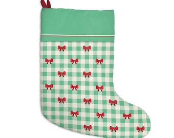 May include: A Christmas stocking featuring a green and white gingham check pattern with small red bows printed throughout. The top section is a solid green band with a thin red and white stripe, and a small red fabric loop is attached to the corner.