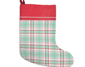 May include: A Christmas stocking featuring a solid red cuff at the top with a thin white horizontal stripe. The main body of the stocking displays a plaid pattern consisting of intersecting lines in shades of mint green, soft pink, white, and red.