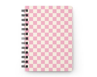 May include: A spiral-bound notebook featuring a repeating checkered pattern of light pink and off-white squares. The notebook is held together by a black metal wire coil along the left side, providing a functional binding for the pages.