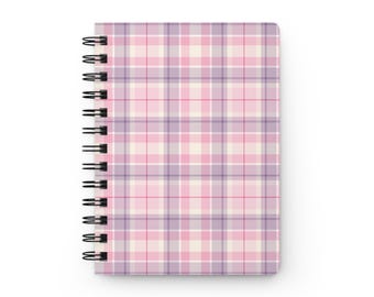 May include: A spiral-bound notebook featuring a plaid pattern in shades of light pink, lavender, and white. The cover displays a grid of intersecting horizontal and vertical lines, with a black metal wire coil binding along the left side.