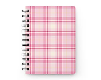 May include: A spiral-bound notebook featuring a plaid pattern in shades of light pink, dark pink, and white with thin yellow intersecting lines. The notebook has a black metal wire binding along the left side and a rectangular shape.