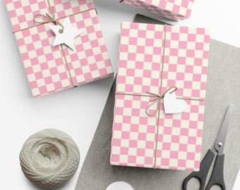 May include: Three rectangular gifts wrapped in pink and white checkered paper, tied with brown twine. Each gift features a blank white paper tag in the shape of a star or heart. A ball of twine, scissors, and blank white tags are nearby.