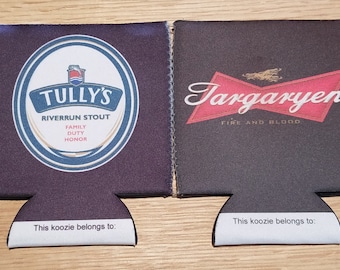 May include: Two black neoprene can coolers with white text and logos. The left cooler features a blue and white logo with the text "Tully's Riverrun Stout Family Duty Honor". The right cooler features a red and white logo with the text "Targaryen Fire and Blood". Both coolers have a white tag at the bottom that says "This koozie belongs to:"