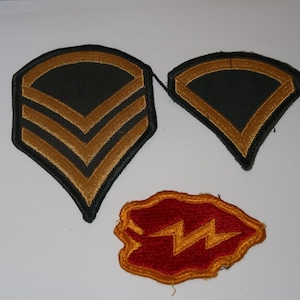 May include: Three embroidered military patches. One large black patch features three gold chevrons. A smaller black patch displays a single gold chevron. A third patch is red with an irregular shape and a gold lightning bolt design in the center.