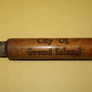 May include: A wooden tool with a metal tip, engraved with the words "City of Grand Island".