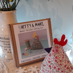 Puede incluir: Un kit de costura para hacer un peluche de pollo. El kit incluye tela, relleno e instrucciones. La caja es marr&oacute;n con texto blanco que dice "Betty & Mabel Mabel Chicken Sewing Kit". El texto "Ain't nobody here but us chicks" est&aacute; impreso en la caja. El texto "Recycle...Design...Create" est&aacute; impreso en la caja. Se muestra un peluche de pollo terminado en la imagen.