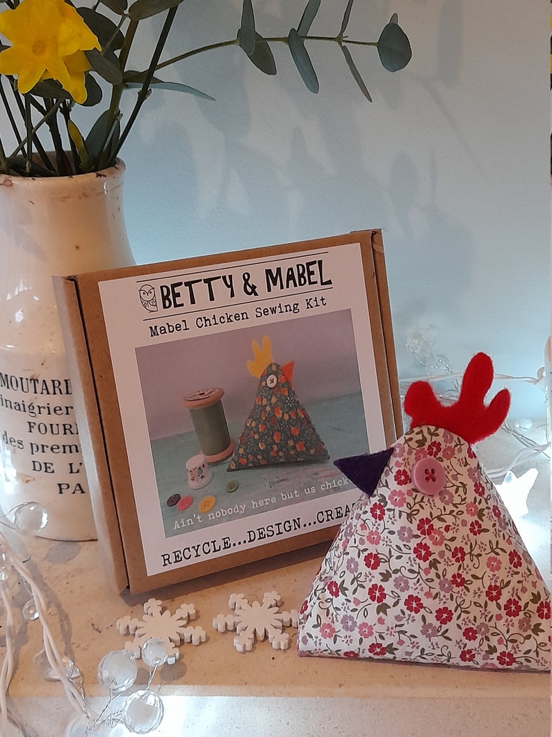 Puede incluir: Un kit de costura para hacer un peluche de pollo. El kit incluye tela, relleno e instrucciones. La caja es marr&oacute;n con texto blanco que dice "Betty & Mabel Mabel Chicken Sewing Kit". El texto "Ain't nobody here but us chicks" est&aacute; impreso en la caja. El texto "Recycle...Design...Create" est&aacute; impreso en la caja. Se muestra un peluche de pollo terminado en la imagen.