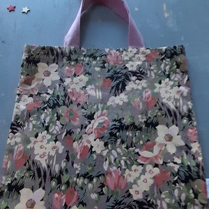 Könnte beinhalten: Eine Blumentasche mit einem rosa-weißen Blumenmuster auf schwarzem Hintergrund. Die Tasche hat einen rosa Stoffgriff.