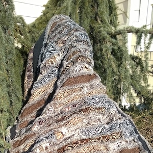 Pode incluir: Uma colcha de retalhos em listras marrons, pretas e brancas com uma borda preta. A colcha é feita de vários tecidos de estampa animal, incluindo leopardo, zebra e tigre.