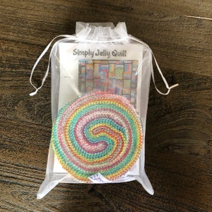 May include: A white organza bag containing a colourful jelly roll fabric and a printed instruction sheet titled "Simply Jelly Quilt".