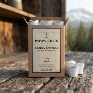 May include: A brown cardboard box of Papaw Bill's Coffee Co. Broken Top Pods with white coffee pods inside and scattered around. The label features an anchor icon, mountain graphic, and text including Brazil-Mexico Blend, Medium Roast, and Net Wt 340g.