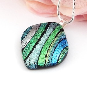 May include: A square-shaped dichroic glass pendant featuring diagonal stripes in shades of metallic silver, emerald green, and bright blue. The pendant is suspended from a silver-toned snake chain necklace, showcasing a reflective and textured surface.