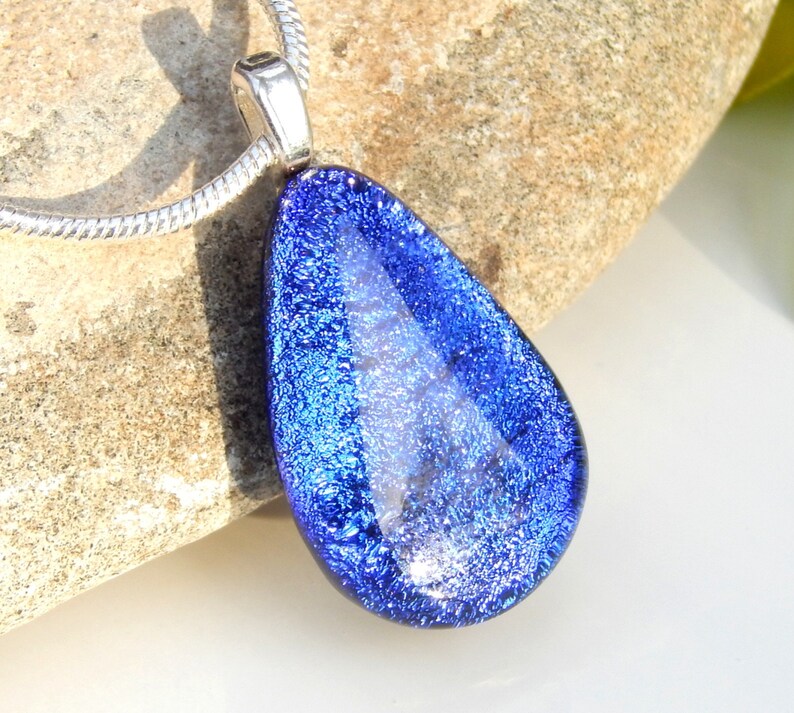 Puede incluir: Un collar con un colgante en forma de l&aacute;grima de vidrio azul. El vidrio tiene un acabado brillante e iridiscente.